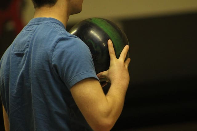 Close up shot from behind man in t-shirt holding bowling ball
