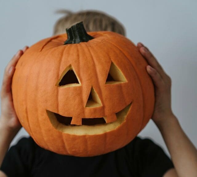 Kid holding carved jack-o-lantern in front of face